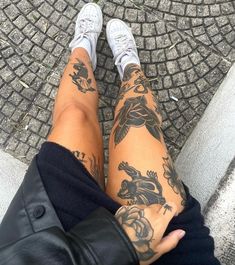 a person with tattoos on their legs is sitting in front of a brick walkway and looking down at the ground