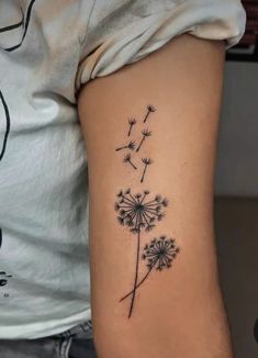 a black and white photo of a dandelion tattoo on the left side of the arm