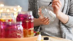 a woman is holding a glass with some liquid in it and writing on the jar