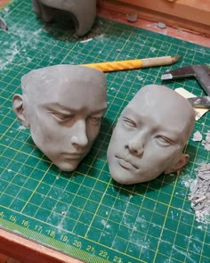 two clay heads sitting on top of a cutting board next to a pair of scissors