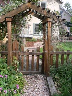 a wooden gate in front of a house with purple flowers growing around it and an arbor