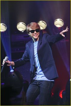 a man in sunglasses and a suit on stage with his arms out to the side