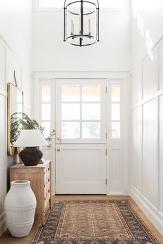 an entryway with a rug, vase and lamp