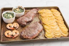 a tray filled with meat, potatoes and shrimp