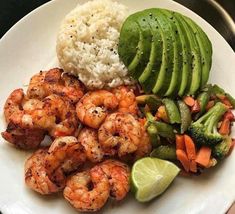 a white plate topped with shrimp, rice and veggies next to an avocado