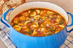 a blue pot filled with pasta soup next to a piece of bread on top of a table