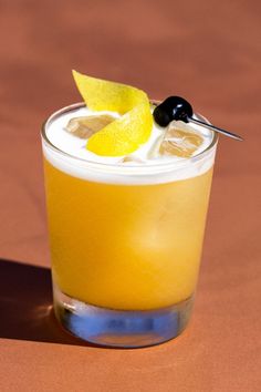 an orange drink with a black olive garnish on the rim and lemon wedge