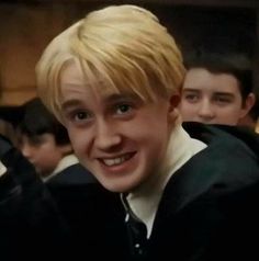 a young man with blonde hair smiles at the camera while other boys stand behind him