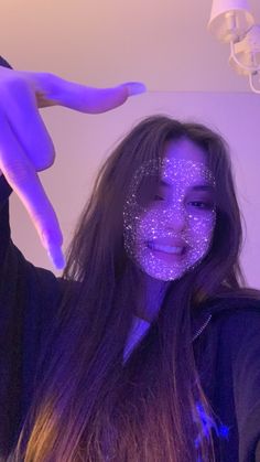 a woman with purple glitter on her face pointing at the camera