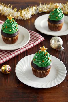 two cupcakes with green frosting and christmas decorations on them sitting on plates