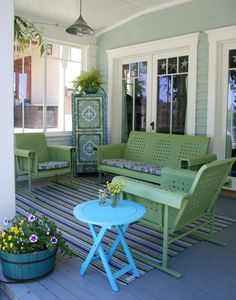 a porch with green furniture and potted plants on the side walk, next to a blue table