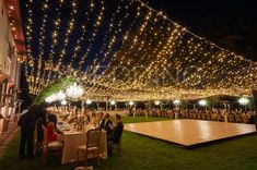 people are sitting at tables with lights strung over the top and on the ground in front of them