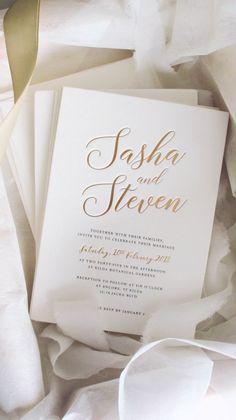 a white and gold wedding card on top of some tissue