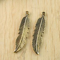 two gold tone feather charms sitting on top of a wooden table