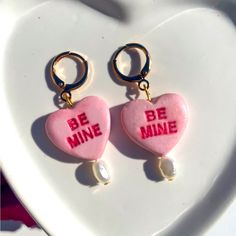 two heart shaped candy earrings with the words be mine written on them in pink and gold