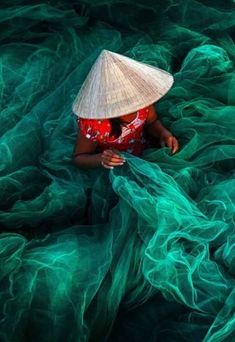 a woman wearing a straw hat and red dress sitting on top of a green net