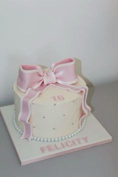 a white cake with pink ribbon and pearls on the top that says felicity