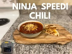 a bowl of chili sitting on top of a wooden cutting board next to a toaster