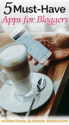 a person holding a cell phone next to a cup of coffee on a wooden table