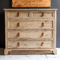 an old wooden dresser with leather handles on it's doors and drawers, in front of a black wall