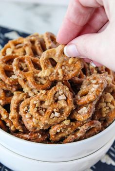 a hand is picking up some pretzels out of a white bowl on a blue and white tablecloth