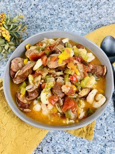 a white bowl filled with shrimp and vegetable stew next to a pine cone on a yellow towel