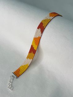 an orange and yellow beaded bracelet on a white cloth with a silver clasp is shown