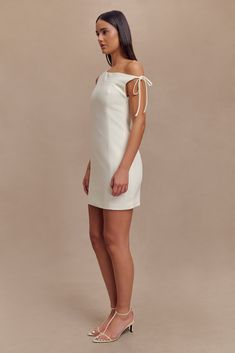 Timeless redesign. The BAKER Suiting Off Shoulder Dress is a perfect blend of modern sophistication and timeless elegance. This mini dress features an asymmetrical neckline and a drop shoulder design, highlighted by a chic shoulder tie detail for added flair. The contour panel lines create a flattering silhouette, while the side zip closure ensures a seamless fit. With its mini length, the Baker dress offers a stylish and polished look, ideal for any upscale event or evening out. White Fitted Mini Dress With Structured Shoulders, Chic Off White A-line Mini Dress, Chic Off-white A-line Mini Dress, Chic White Off-shoulder Asymmetrical Dress, White A-line Mini Dress With Bow, Capsule Wardrobe Accessories, European Summer Outfits, Wardrobe Accessories, Asymmetrical Neckline