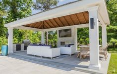 an outdoor kitchen and dining area is shown in this backyard setting, with white furniture on the patio