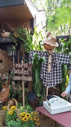 a scarecrow is standing next to a table with plants and other things on it