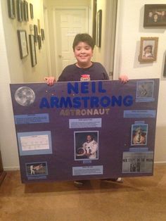 a young boy holding up a sign that says neil armstrong on it in front of a hallway