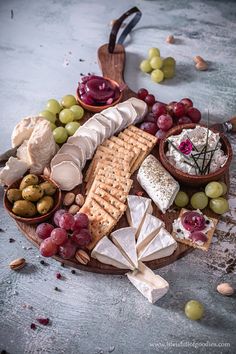 an assortment of cheeses, crackers and grapes on a platter with nuts