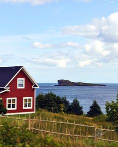 a red house sitting on top of a lush green hillside next to the ocean with an island in the distance