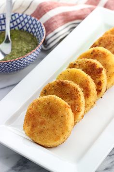 some food is on a white plate and next to a bowl with green sauce in it