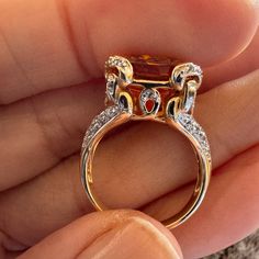 someone is holding an orange ring with diamonds on the sides and two red stones in the middle