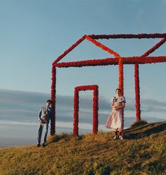 two people standing on top of a hill next to a structure made out of flowers