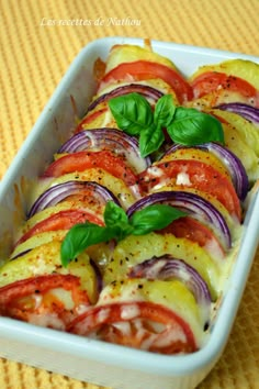 a casserole dish filled with sliced tomatoes, onions and basil garnish