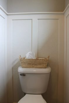 a white toilet sitting in a bathroom next to a basket on the back of it