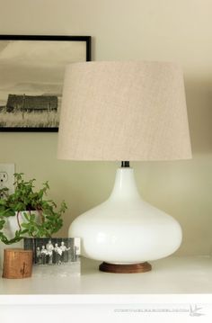 a white lamp sitting on top of a table next to a potted green plant