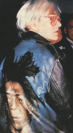 an older man with white hair and glasses wearing a leather jacket in front of another man