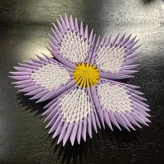 an origami flower with yellow center sitting on top of a wooden table next to a black surface