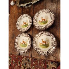 four plates with deer designs on them sitting on a wooden table next to a rug