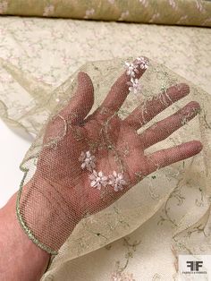 a person's hand with flowers on it is covered in netting and sits next to a bed sheet