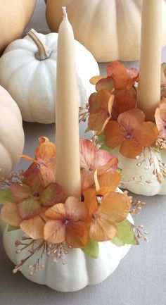 three candles with flowers and leaves on them sitting next to pumpkins in the background