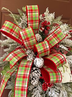 a christmas wreath with pine cones, evergreens and plaid ribbon on the front door