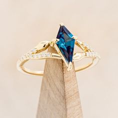 a gold ring with a blue stone and white diamonds on it, sitting on top of a piece of wood