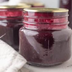 two jars filled with jam sitting on top of a counter next to a towel and spoon