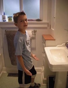 a young boy standing in front of a bathroom sink