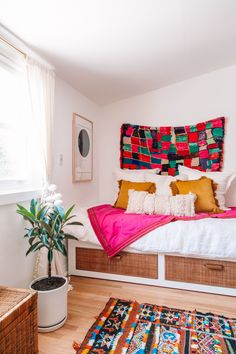 a bed with colorful blankets and pillows in a room next to a potted plant