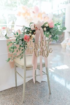 a chair decorated with pink flowers and greenery sits in front of a white table